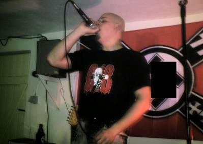 Dennis Zadow (Sänger von "Strafmass") mit "Combat18"-Shirt vor Hakenkreuzflagge und SS-Runen