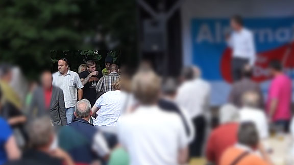 Plate und Begleitung am Rande der AfD-Bühne (Screenshot aus oben verlinktem Video)
